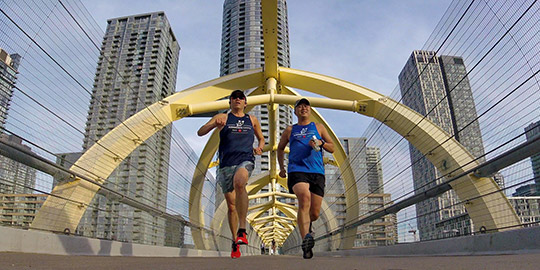 Two Running Rats, running side-by-side north over the Puente de Luz bridge, framed symmetrically by the elaborate yellow steel bridge structure