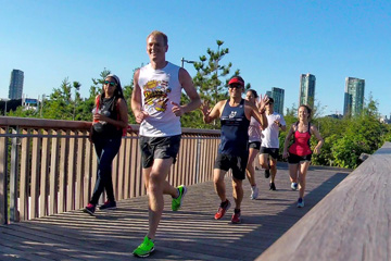 Runners smiling and waving, heading over the wooden bridge at Trillium Park