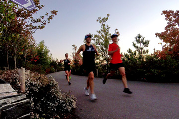 Three runners moving through a park at sunset, too quickly to keep in focus