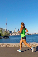 A woman running along the water's edge in the summertime, the downtown skyline behind her