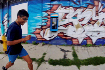 A man running, laughing, past a graffiti mural in the east end of the city